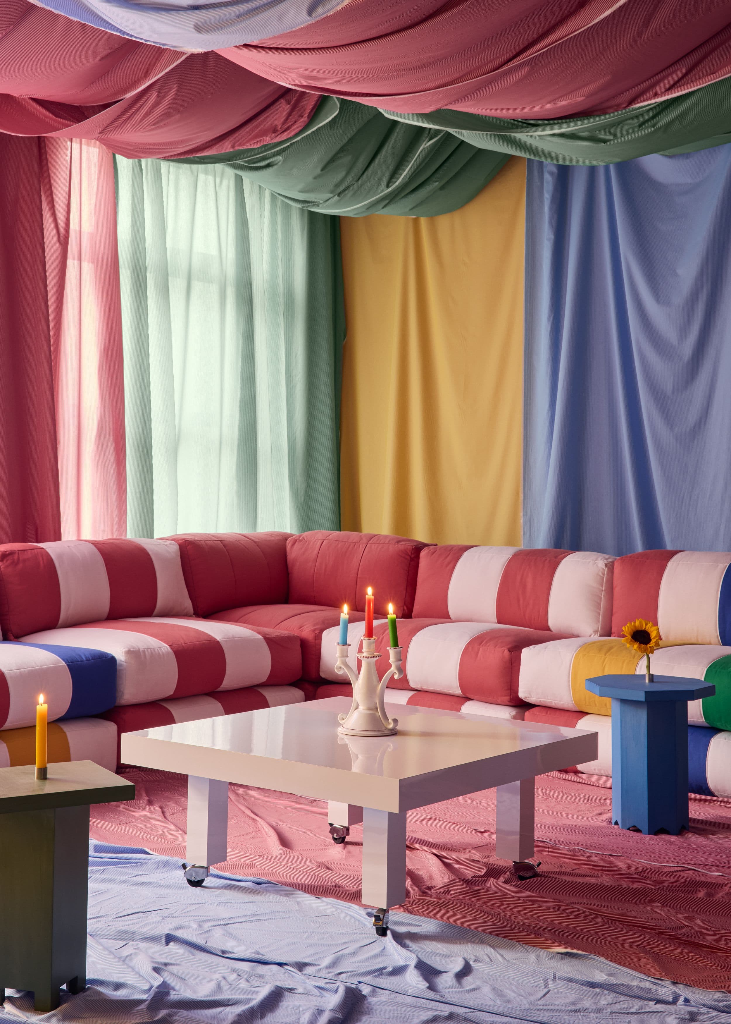 Pink and white striped corner seating with a pale pink table and blue side table, framed by colorful fabric draping