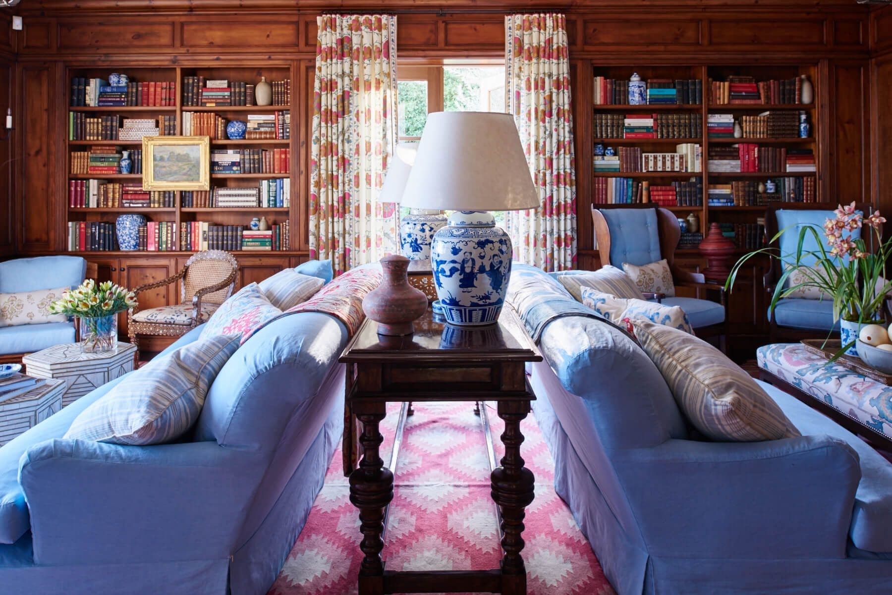 Blue upholstered sofa and chairs with red patterned drapery in the library
