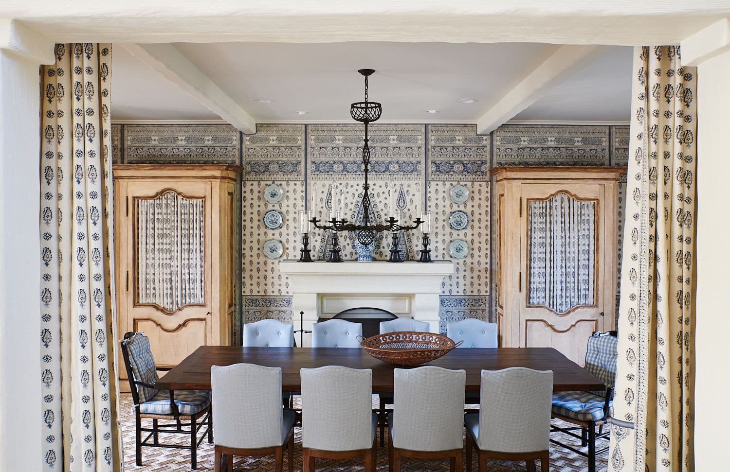 Armoire with paisley-patterned covers, tufted dining room chairs, and space-sectioning drapery
